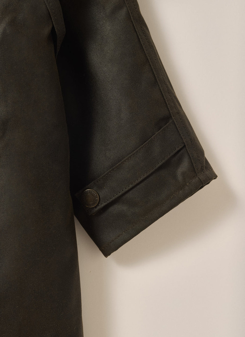 Close-up of Driza-Bone Kids Rider Coat sleeve showing durable cuff stitching, weatherproof oilskin finish, and classic brass snap fastener.