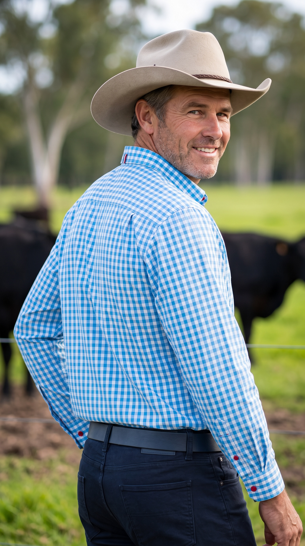 Rear three-quarter view of model wearing S.Kidman Holstein Long Sleeve Shirt in Pale Blue gingham in a rural setting.