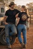 Australian rural couple wearing the black Outback Clothing Co OCC Muster Tee beside a Toyota LandCruiser at a cattle station, showing the front chest logo and large back artwork.