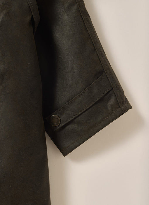 Close-up of Driza-Bone Kids Rider Coat sleeve showing durable cuff stitching, weatherproof oilskin finish, and classic brass snap fastener.