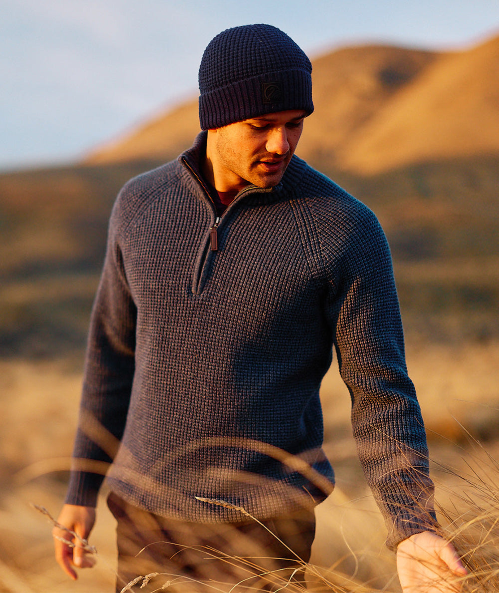 Man wearing a dark sweater and Newton Navy Blue knit beanie standing in a field with mountains in the background.