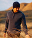 Man wearing a dark sweater and Newton Navy Blue knit beanie standing in a field with mountains in the background.