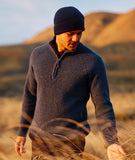Man wearing a dark sweater and Newton Navy Blue knit beanie standing in a field with mountains in the background.
