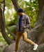 Man in plaid shirt and beige pants walking on a tree trunk in a forest wearing Newton Navy Blue Beanie