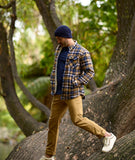 Man in plaid shirt and beige pants walking on a tree trunk in a forest wearing Newton Navy Blue Beanie